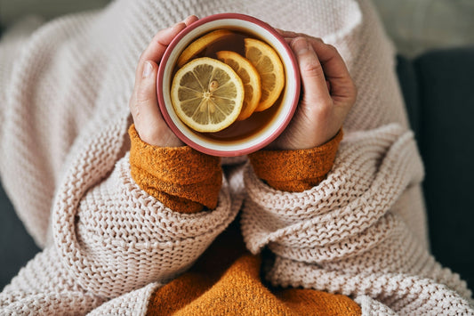 Hands holding hot tea with lemon and wrapped in blanket.
